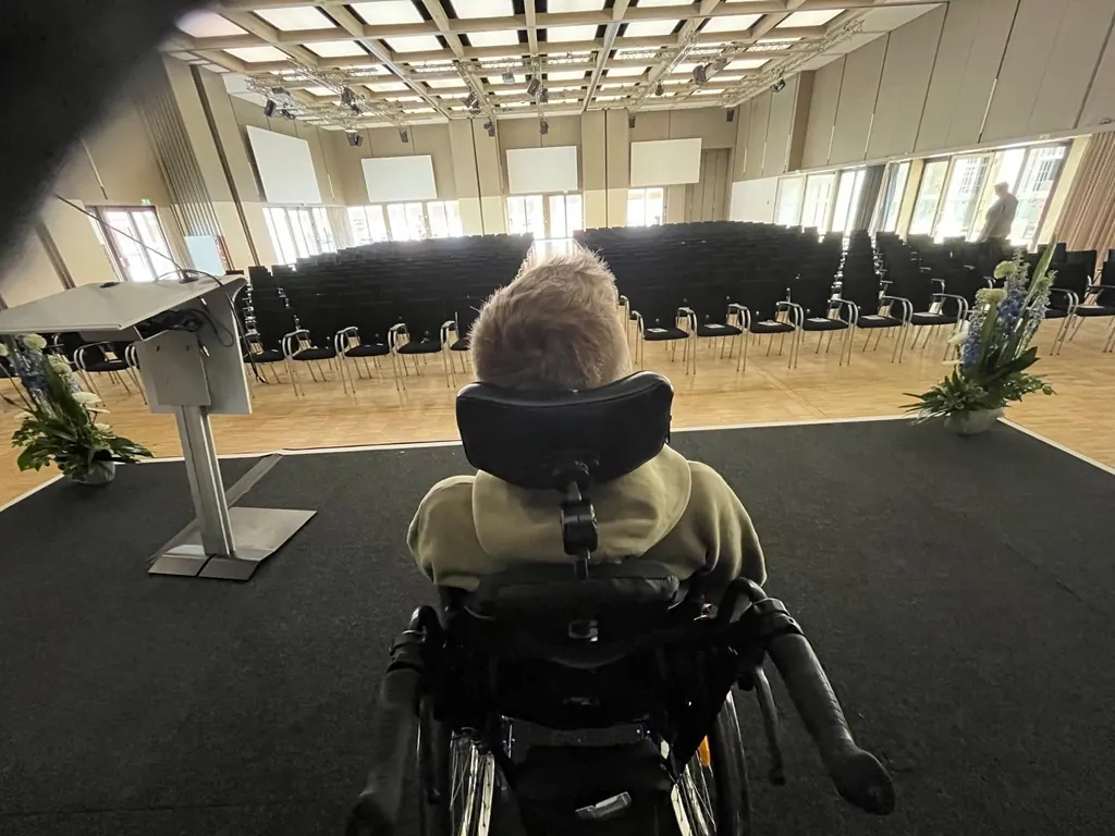 Ich blicke von der Bühne aus auf die Stuhlreihen eines Veranstaltungssaals.