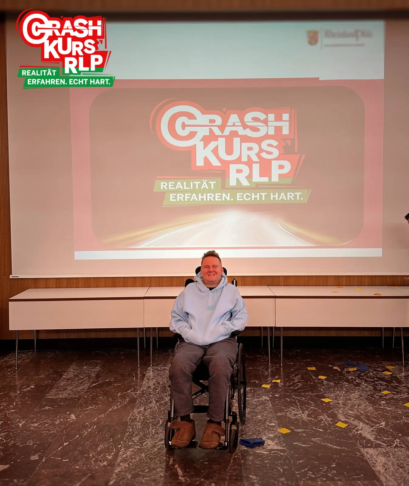 Ich spreche auf einer Bühne vor einer Leinwand mit der Aufschrift Crash Kurs RLP.
